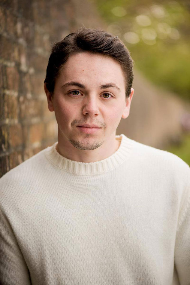 young man in cream jumper leans on wall