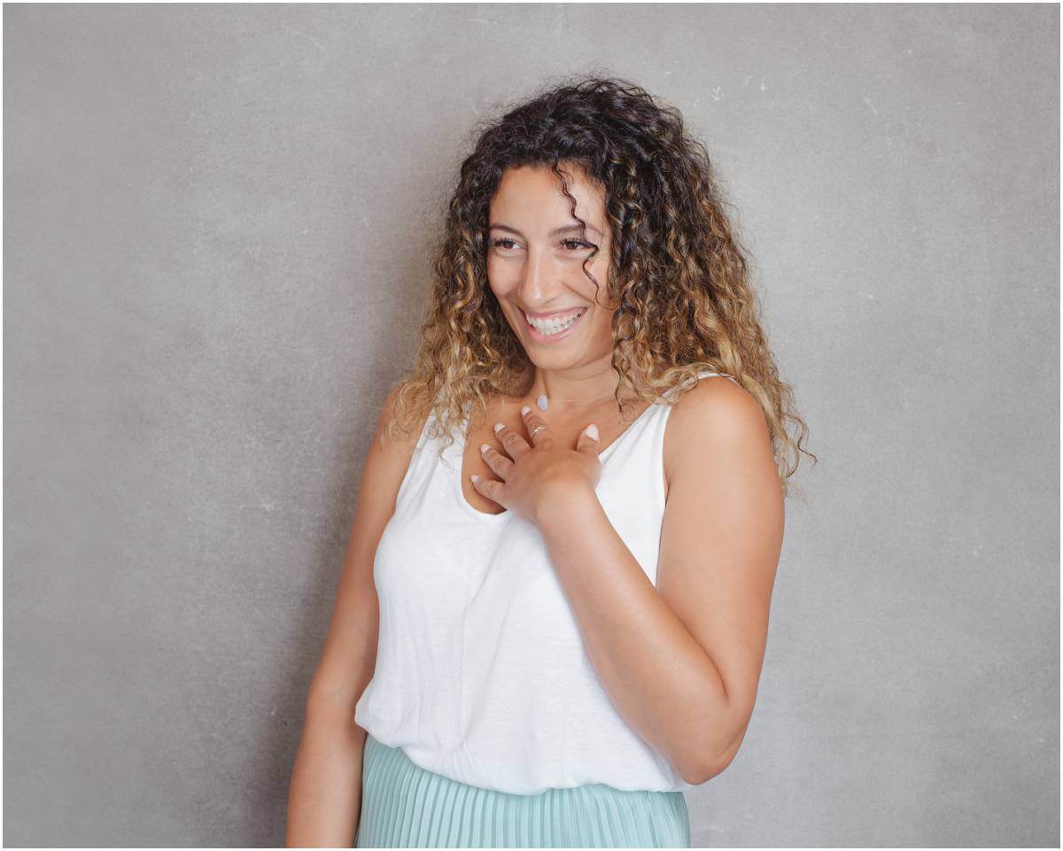 Professional LinkedIn headshot of an attractive woman in a blue skirt against a grey background, capturing a spontaneous laugh in an in-between moment
