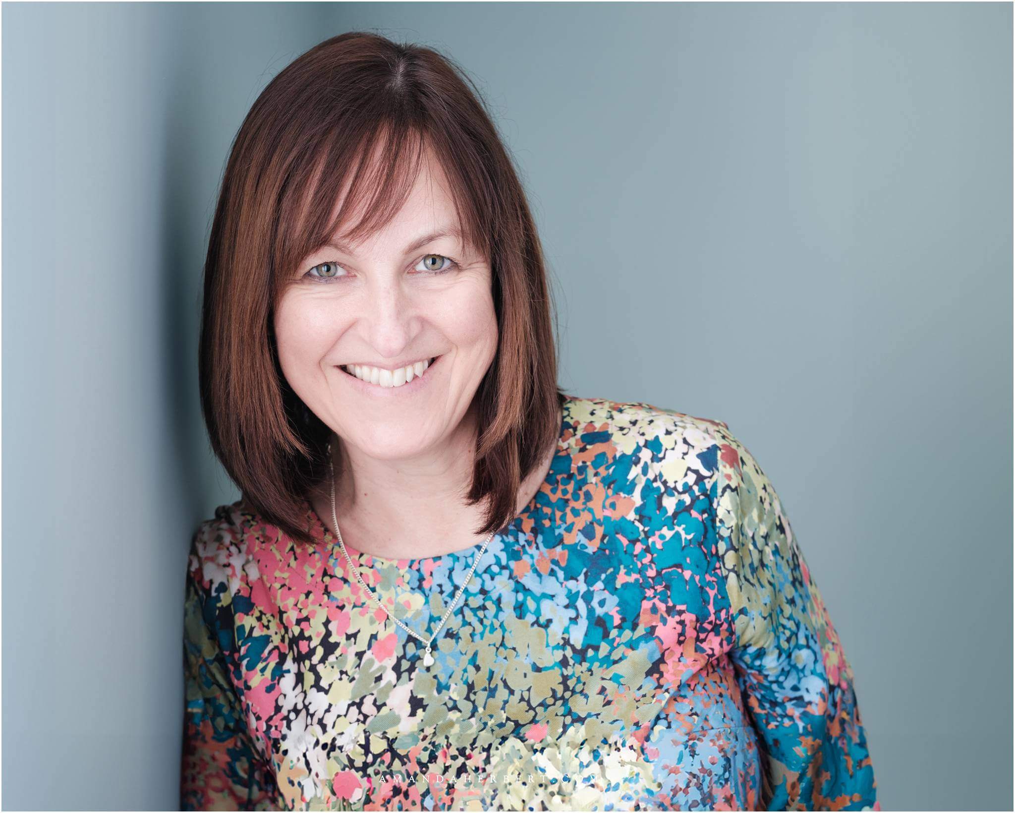 Corporate photography services: Happy financial director smiling against a blue wall